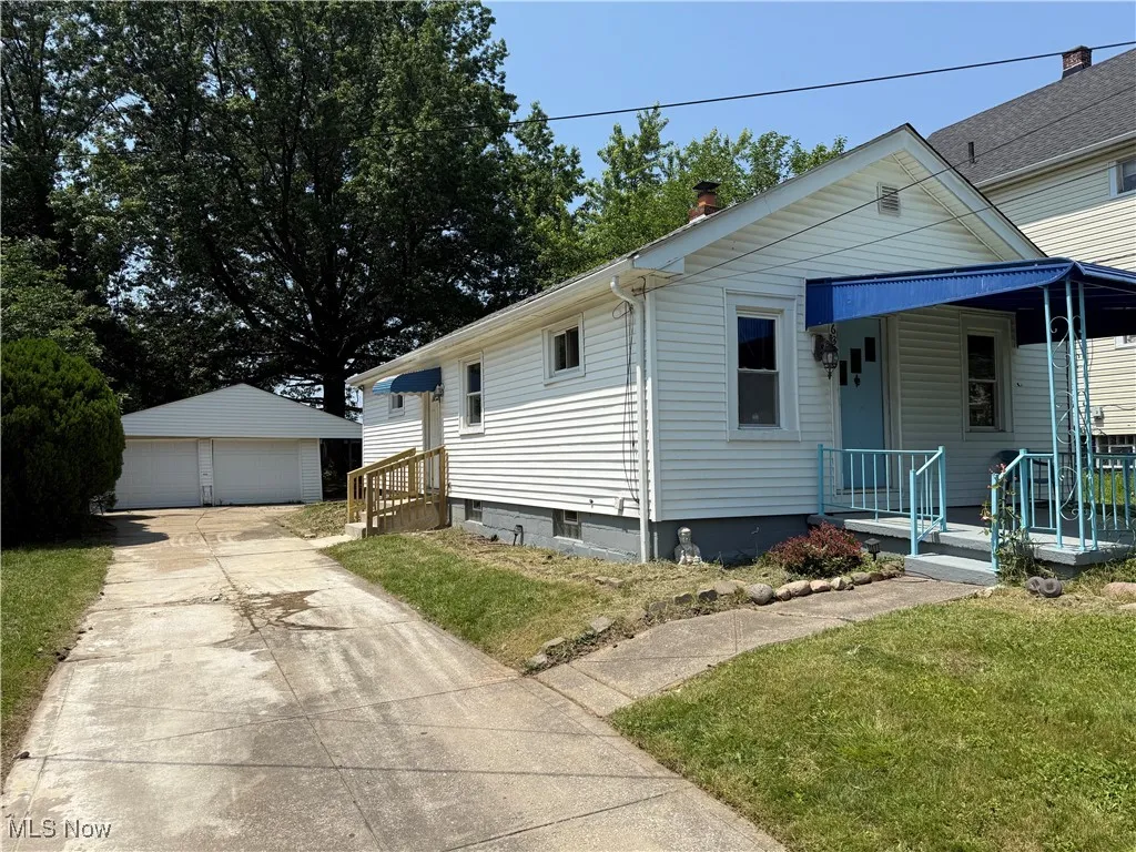 View of front of property with a detached garage, an outdoor structure, and a front lawn