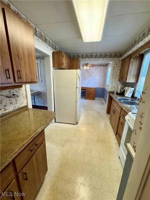 Kitchen featuring wallpapered walls, white appliances, light flooring, and brown cabinetry