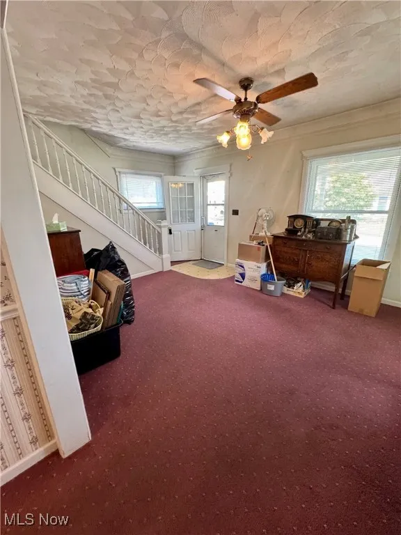 Sitting room with stairway, carpet flooring, a ceiling fan, and ornamental molding