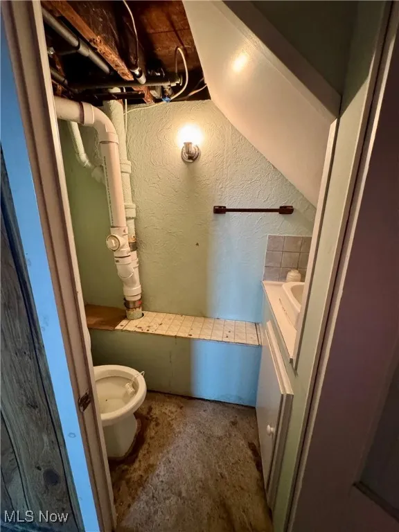 Bathroom with vanity, unfinished concrete floors, and a textured wall