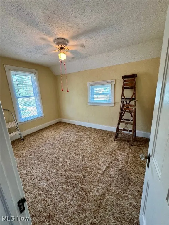 Carpeted empty room featuring a textured ceiling, lofted ceiling, and a ceiling fan