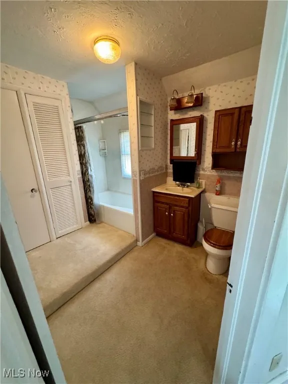 Bathroom featuring vanity, a textured ceiling, shower / bath combo, and wallpapered walls