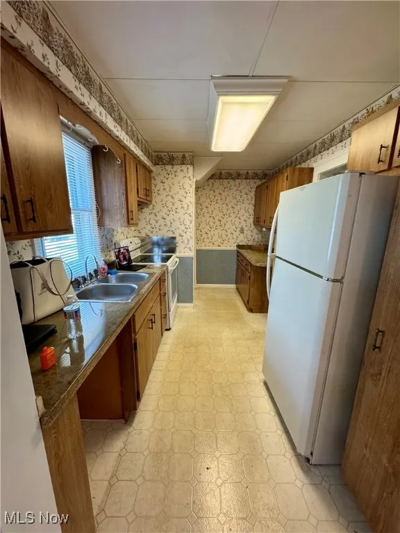 Kitchen featuring white appliances, wallpapered walls, light floors, and brown cabinets