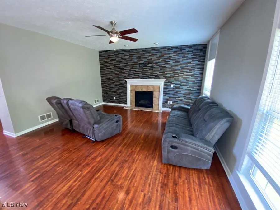 Unfurnished living room with a ceiling fan, wood finished floors, and a tile fireplace