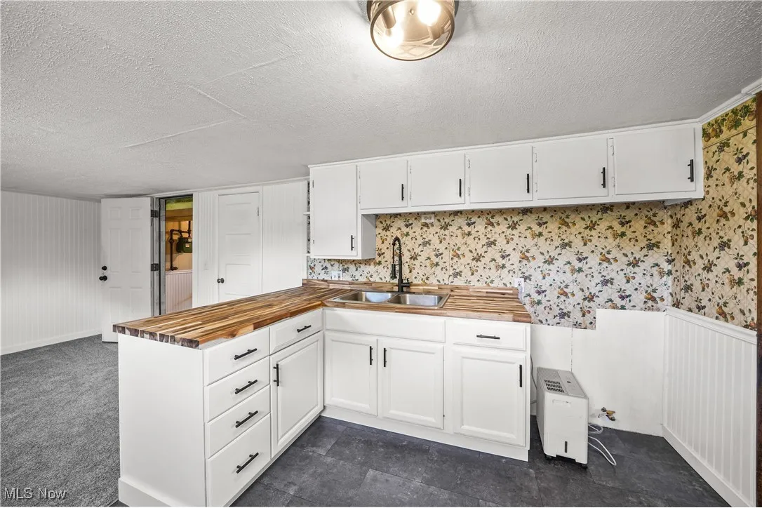 Kitchen featuring wood counters, a textured ceiling, a peninsula, white cabinetry, and wallpapered walls