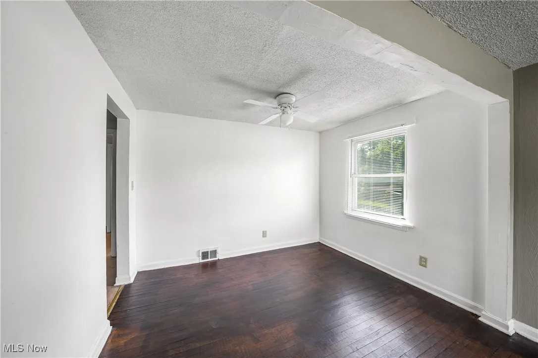 Empty room with ceiling fan, a textured ceiling, and wood-type flooring