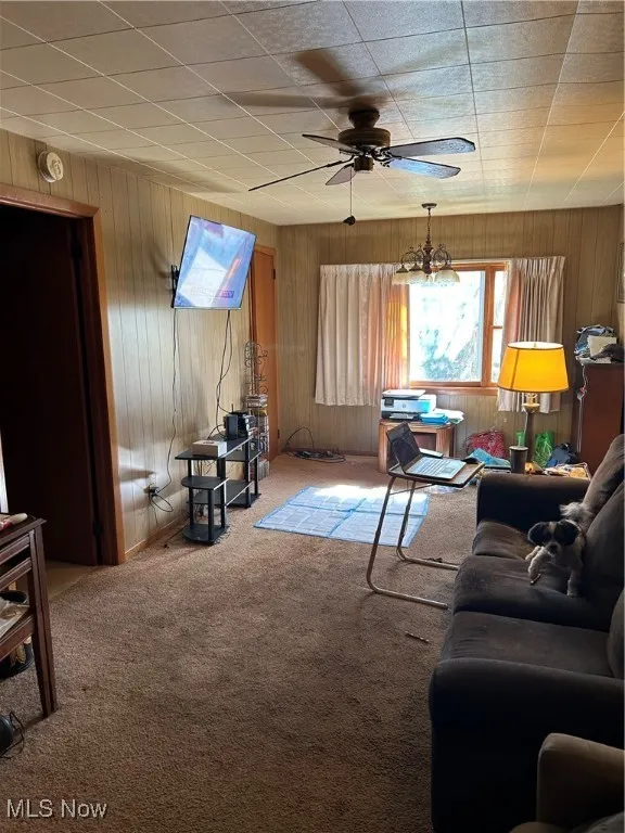 Carpeted living room with ceiling fan and wooden walls