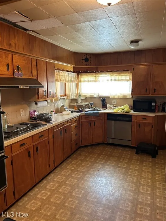 Kitchen with dishwashing machine, ventilation hood, brown cabinets, light flooring, and wooden walls