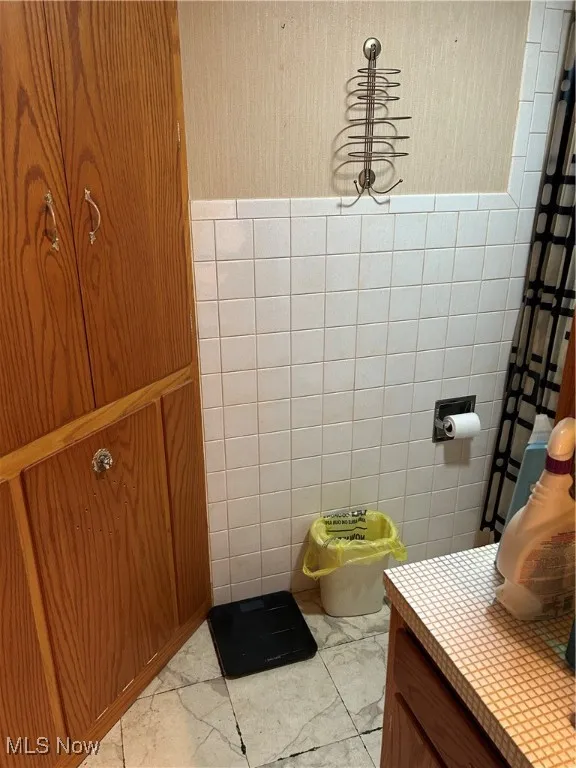 Bathroom with marble finish flooring, tile walls, and vanity