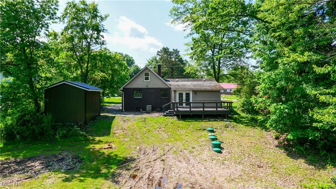 Back of house with a wooden deck, french doors, a storage unit, and a yard