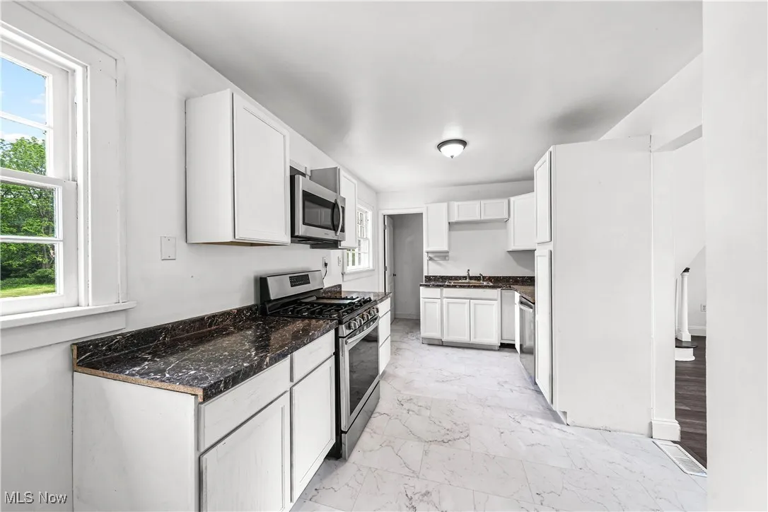 Kitchen featuring appliances with stainless steel finishes, healthy amount of natural light, light marble finish flooring, and white cabinetry