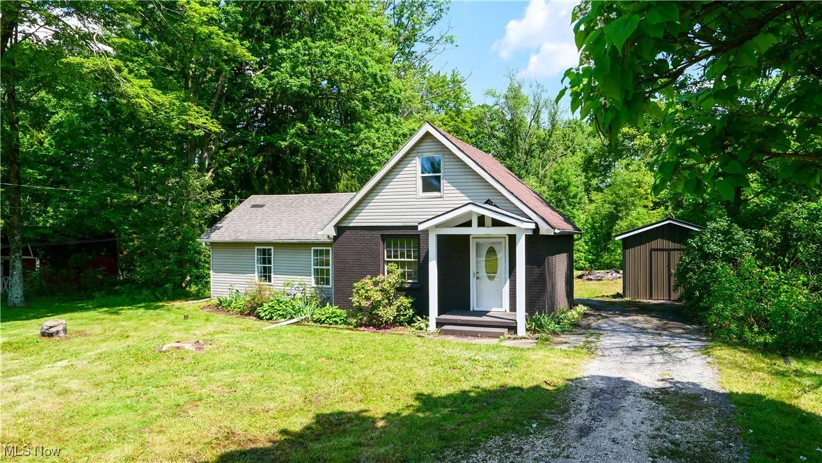 View of front of property with a storage shed, a front yard, driveway, and roof with shingles