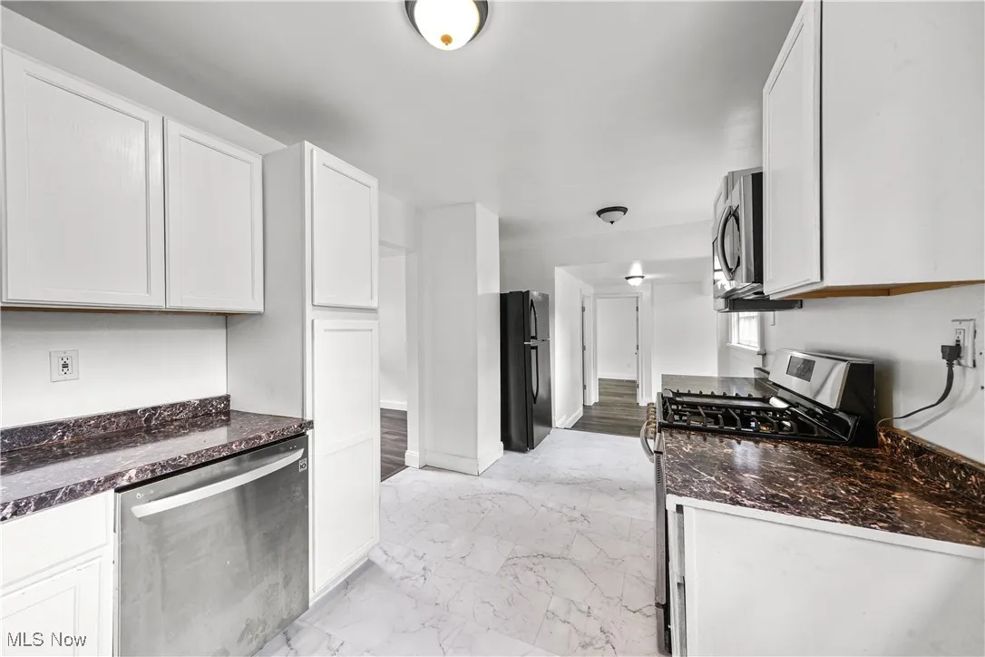 Kitchen featuring appliances with stainless steel finishes, light marble finish flooring, white cabinets, and dark stone countertops