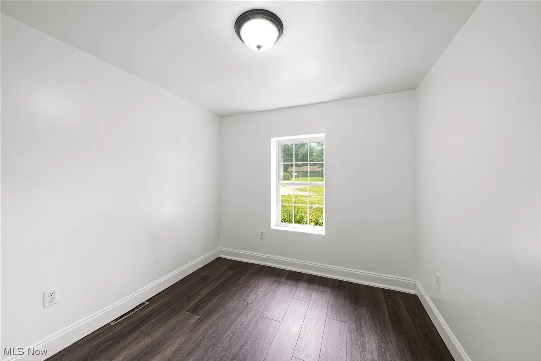 Empty room featuring baseboards and dark wood-style floors