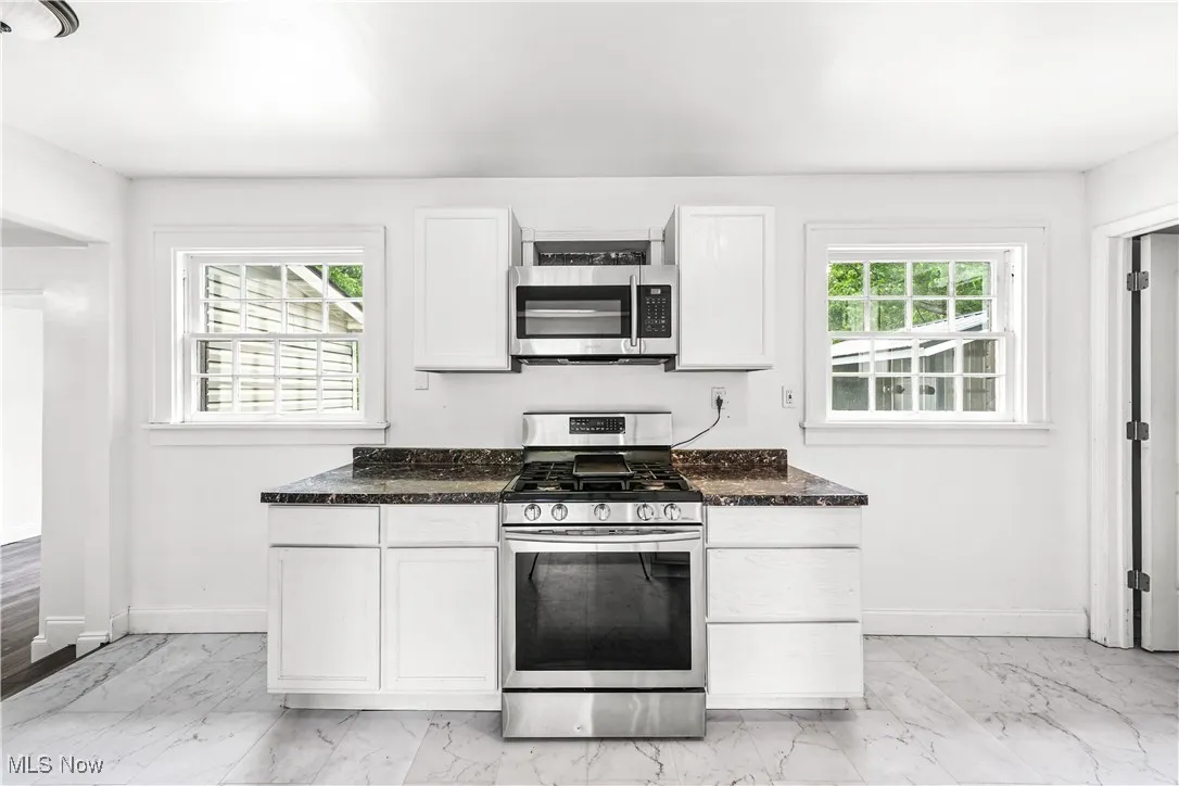 Kitchen with appliances with stainless steel finishes, healthy amount of natural light, light marble finish flooring, and dark stone counters