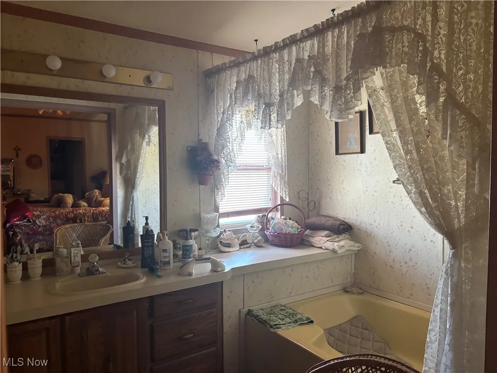 Bathroom featuring wallpapered walls, a tub to relax in, and vanity