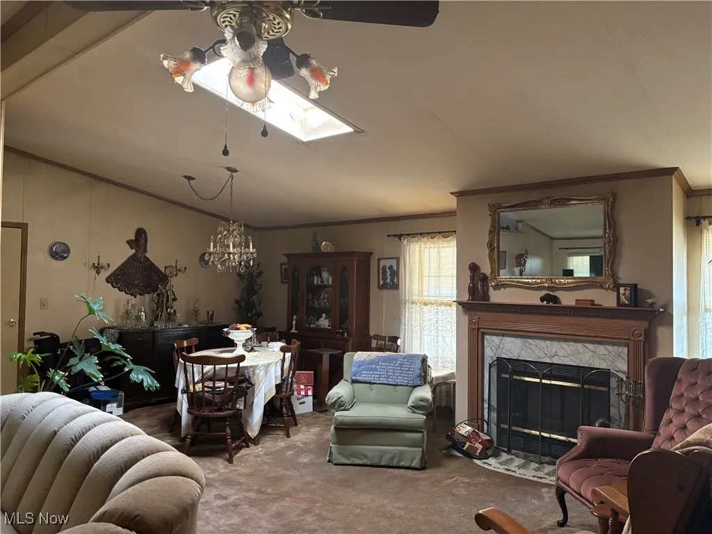 Carpeted living room featuring ornamental molding, lofted ceiling, a skylight, a premium fireplace, and a chandelier