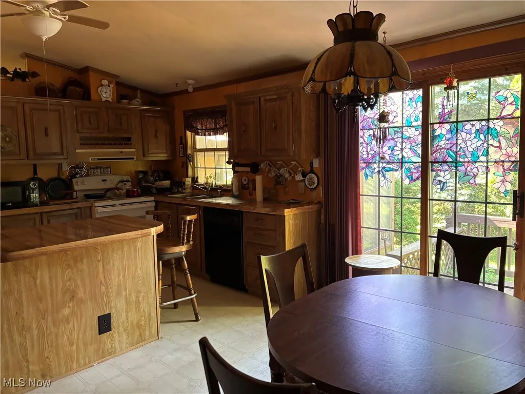 Kitchen with exhaust hood, light floors, black appliances, a chandelier, and lofted ceiling