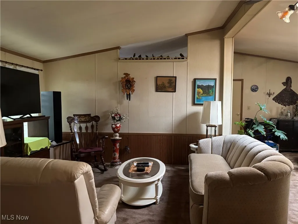 Living area with a wainscoted wall, ornamental molding, and wooden walls