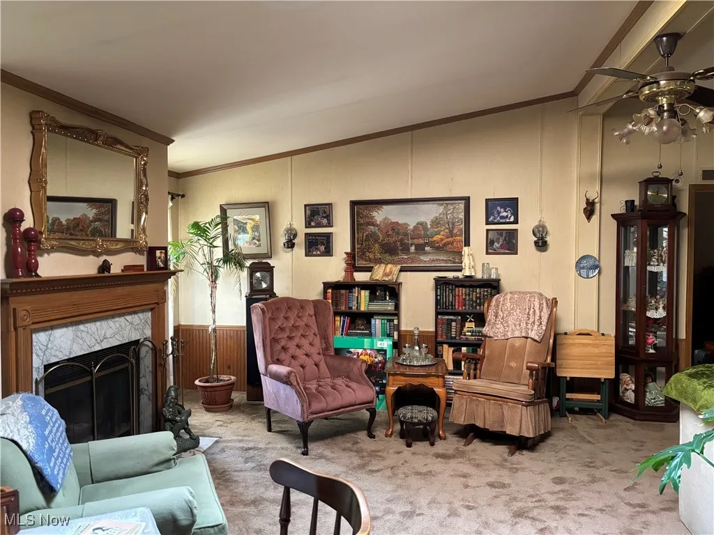 Carpeted living room featuring lofted ceiling, ceiling fan, a fireplace, and ornamental molding