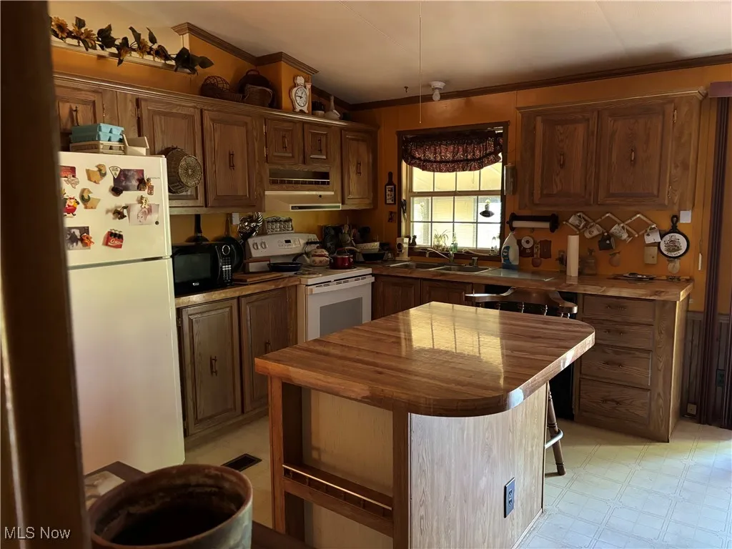 Kitchen with white appliances, butcher block counters, crown molding, vaulted ceiling, and a kitchen island