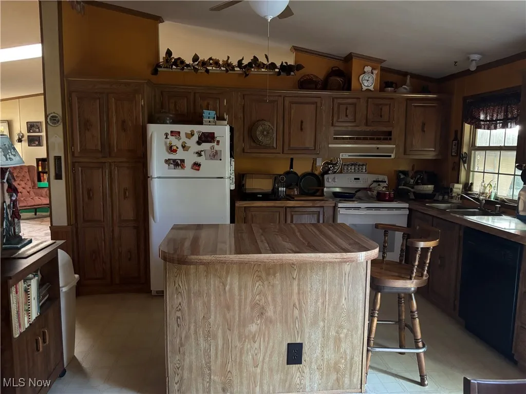 Kitchen with white appliances, lofted ceiling, a center island, range hood, and a ceiling fan