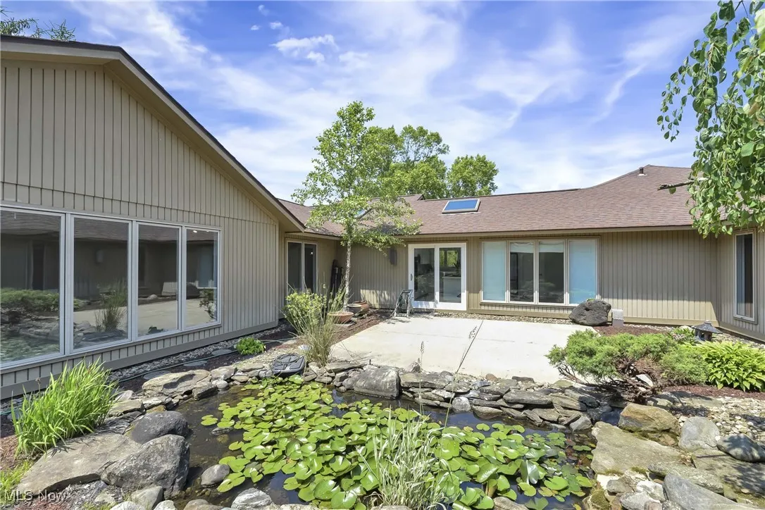 Rear view of property featuring a patio, a small pond, and roof with shingles