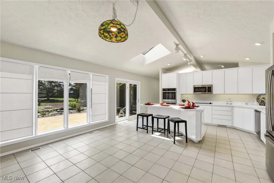 Kitchen featuring stainless steel appliances, lofted ceiling, track lighting, a textured ceiling, and a kitchen island