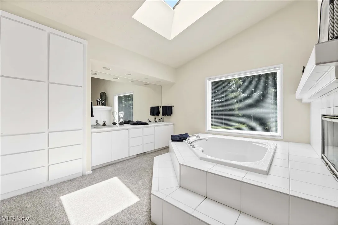 Bathroom featuring double vanity, a garden tub, vaulted ceiling, and a skylight