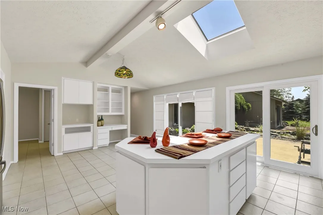 Kitchen with light tile patterned floors, a skylight, white cabinetry, light countertops, and a center island
