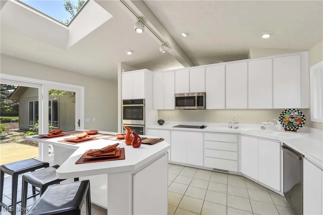 Kitchen with stainless steel appliances, light countertops, a skylight, light tile patterned flooring, and rail lighting