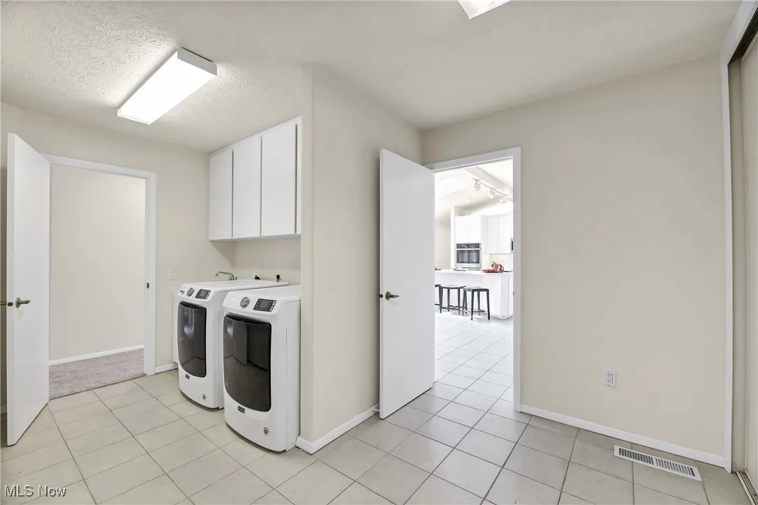 Laundry room with cabinet space, independent washer and dryer, light tile patterned floors, and a textured ceiling