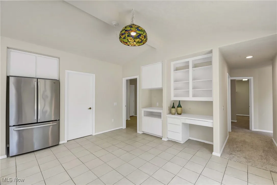 Kitchen featuring freestanding refrigerator, vaulted ceiling, white cabinetry, light tile patterned flooring, and light countertops