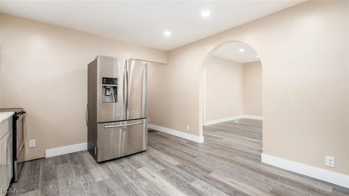 Kitchen with appliances with stainless steel finishes, arched walkways, light wood finished floors, and recessed lighting