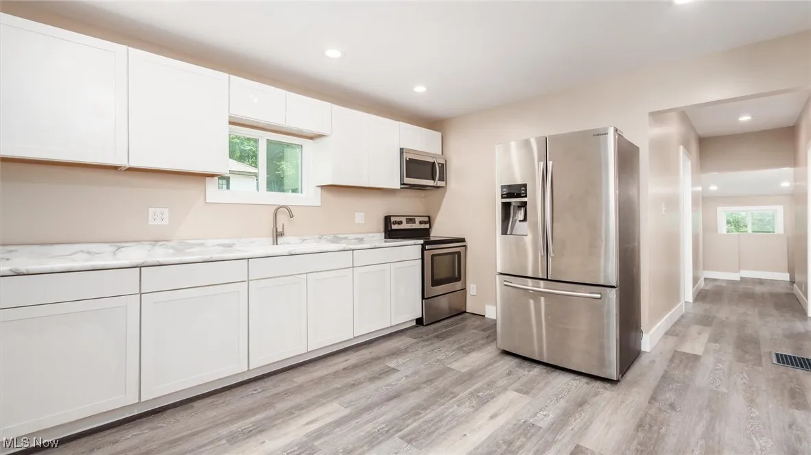 Kitchen with stainless steel appliances, light wood-style flooring, recessed lighting, and white cabinetry