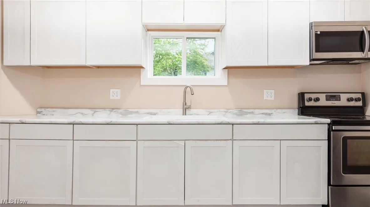 Kitchen with stainless steel appliances, white cabinetry, and light stone counters