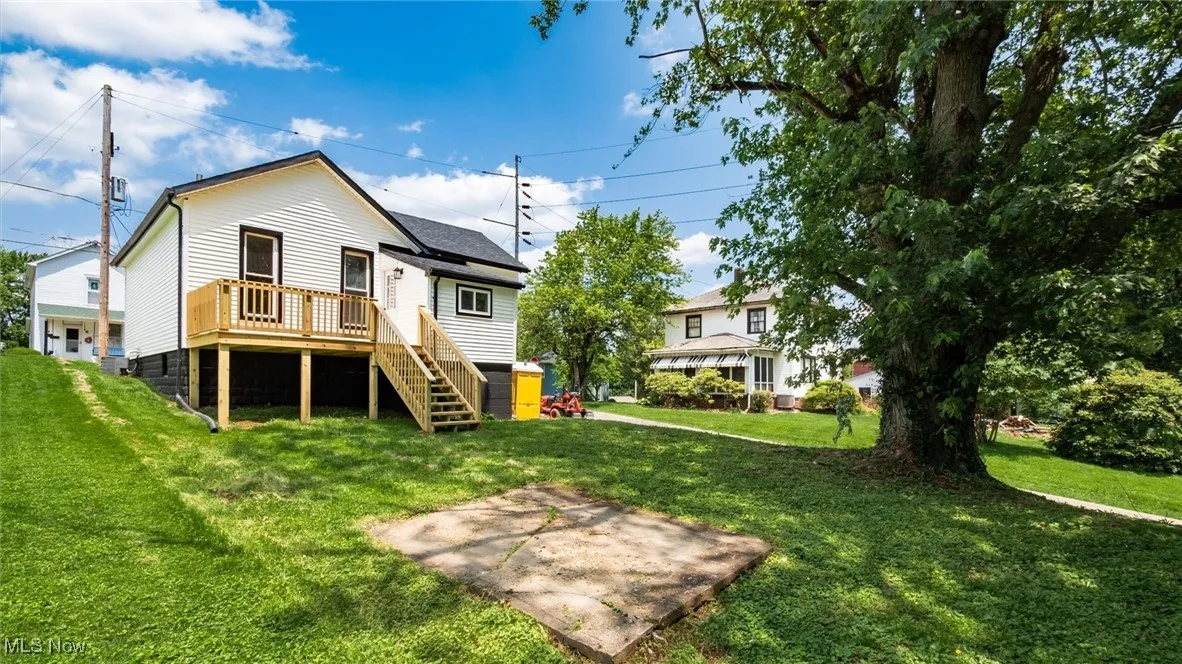 Rear view of property featuring stairs, a lawn, and a wooden deck