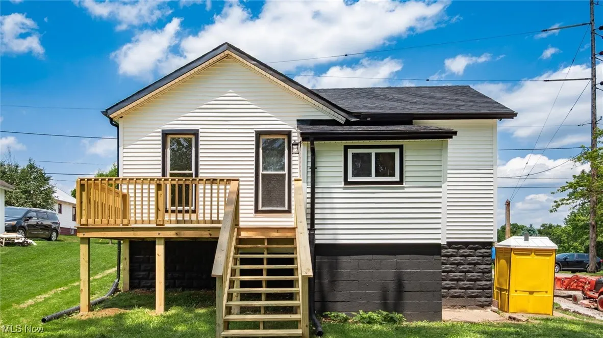 Back of property with a deck, a shingled roof, a lawn, and stairs