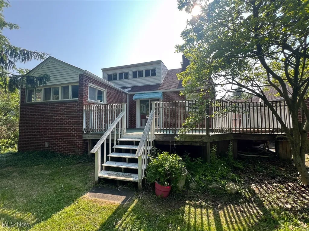 Rear view of house with brick siding, a wooden deck, a lawn, and crawl space
