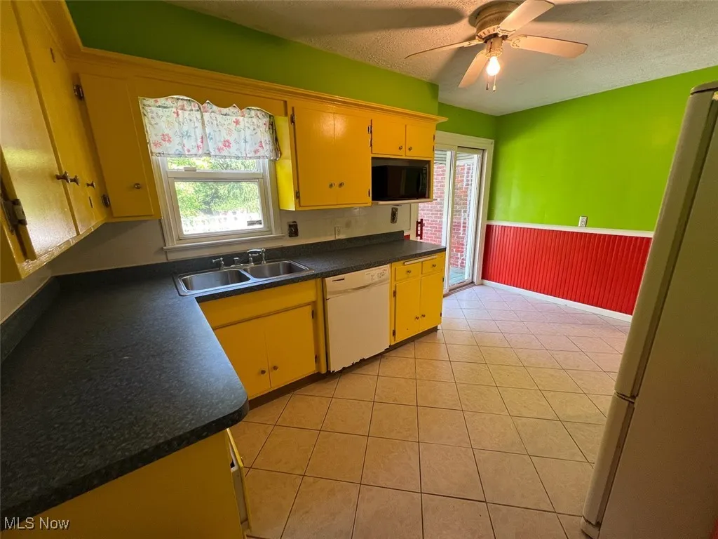 Kitchen with white appliances, wainscoting, dark countertops, a ceiling fan, and a textured ceiling