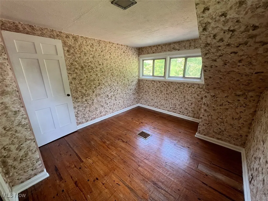 Bedroom featuring dark wood-style flooring, a textured ceiling, and wallpapered walls