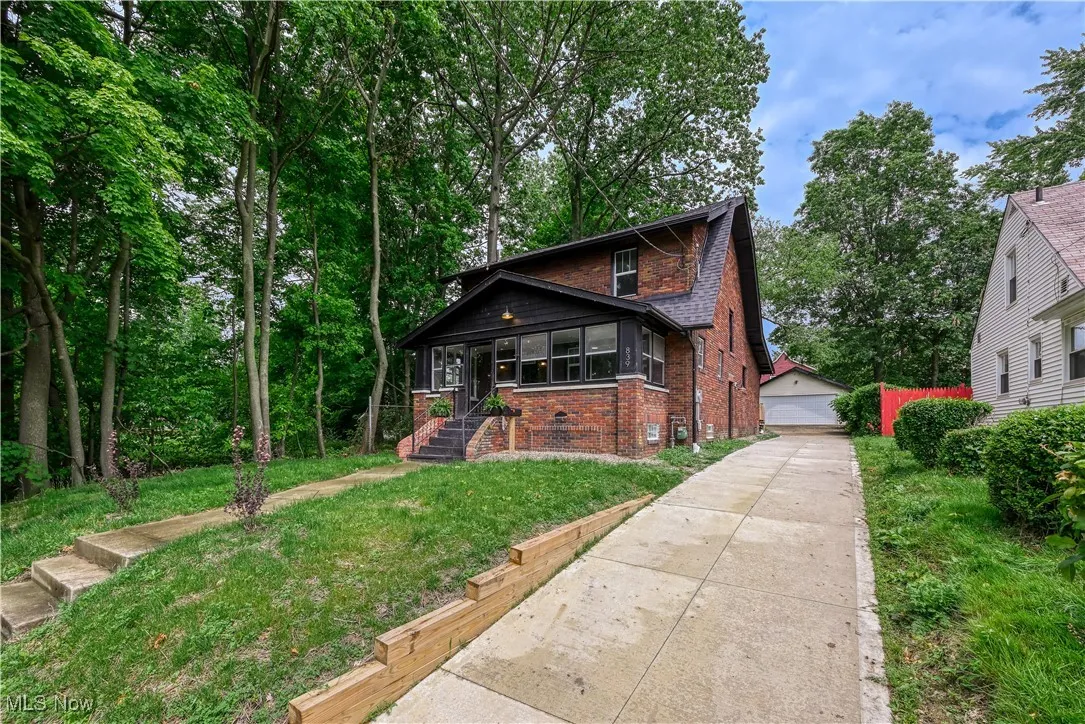 Bungalow-style house with brick siding, a detached garage, an outdoor structure, and a front lawn