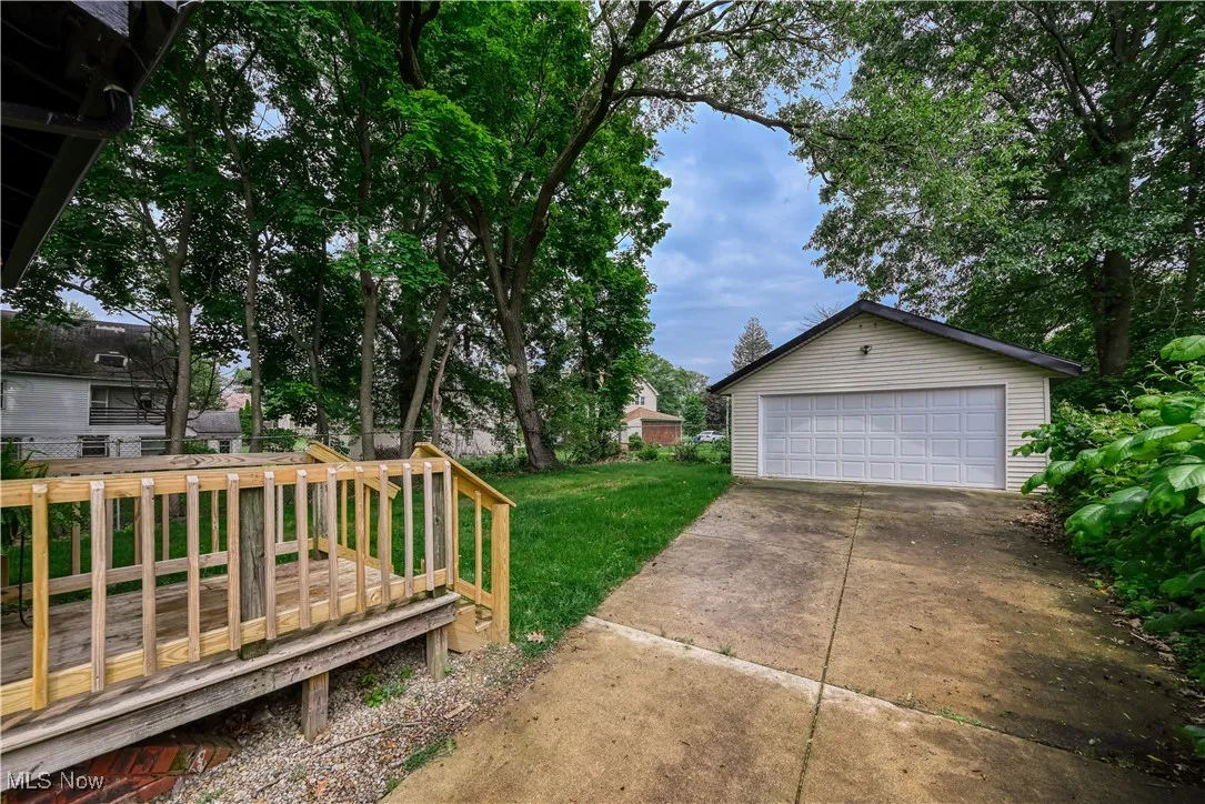 View of green lawn with an outbuilding, a detached garage, and a deck