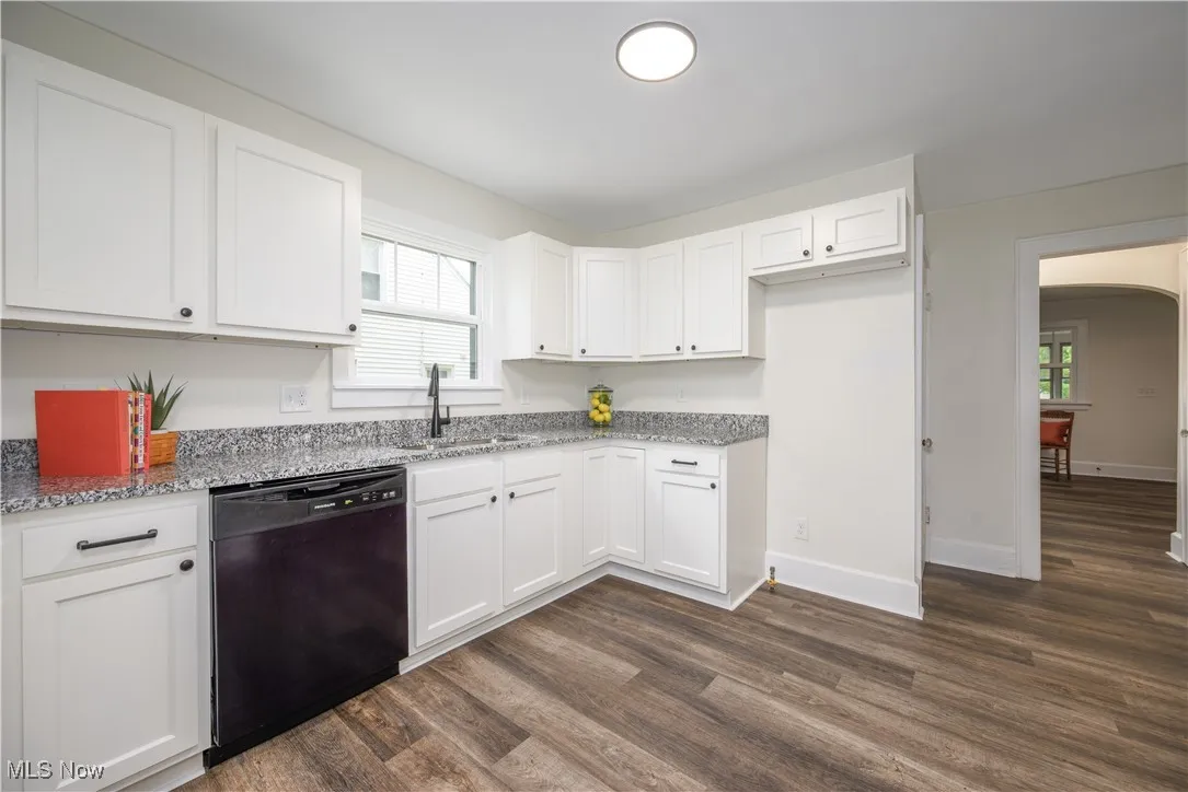 Kitchen featuring black dishwasher, dark wood finished floors, arched walkways, light stone counters, and white cabinetry
