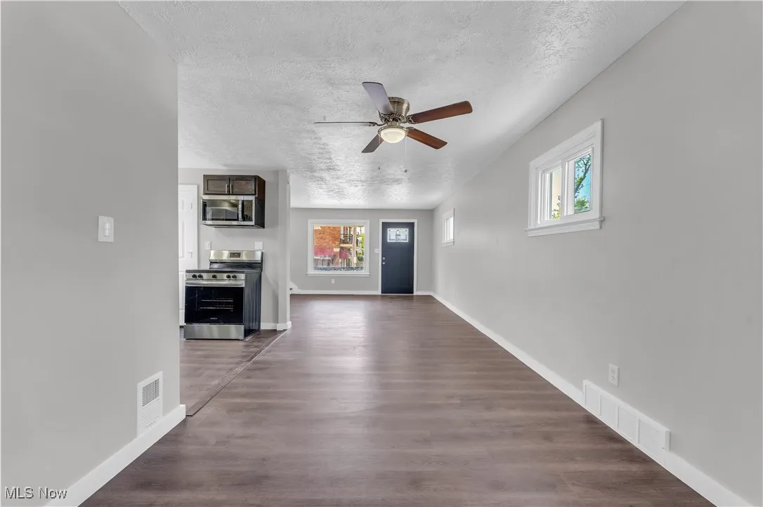 Unfurnished living room with a textured ceiling, healthy amount of natural light, a ceiling fan, and dark wood-style floors