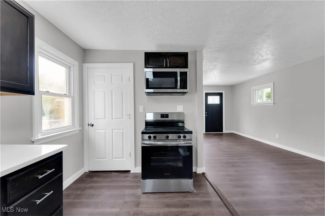 Kitchen featuring appliances with stainless steel finishes, a textured ceiling, dark wood-type flooring, and light countertops