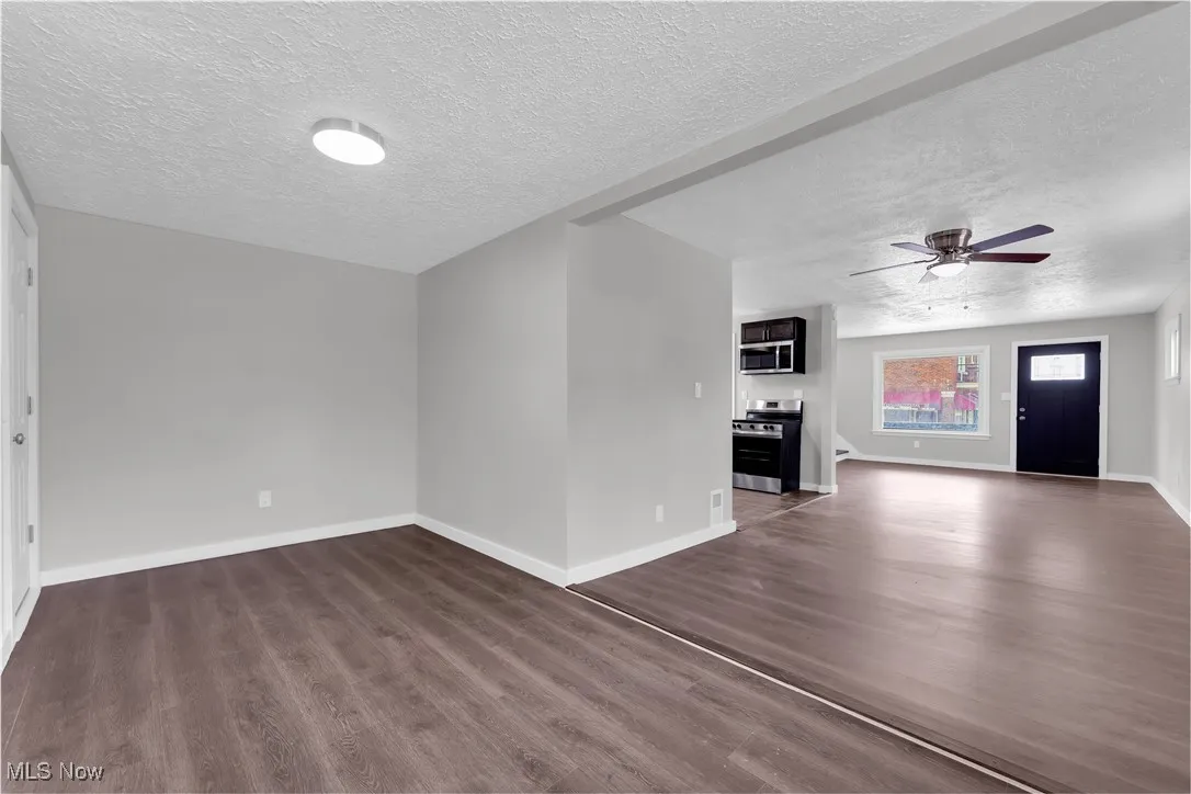 Unfurnished living room with a textured ceiling, dark wood-style flooring, and a ceiling fan