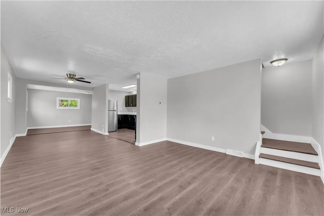 Unfurnished living room with wood finished floors, ceiling fan, a textured ceiling, and stairs