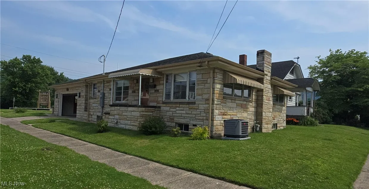 View of side of property with stone siding, a chimney, a yard, and an attached garage