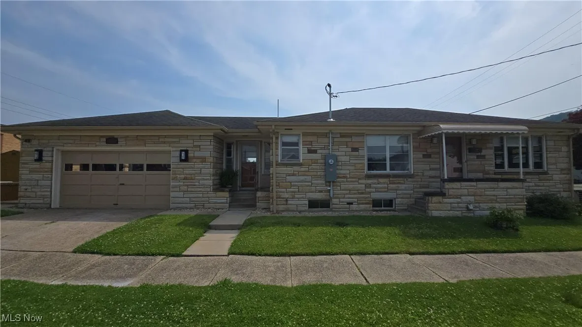 Single story home with a garage, stone siding, concrete driveway, and a front yard